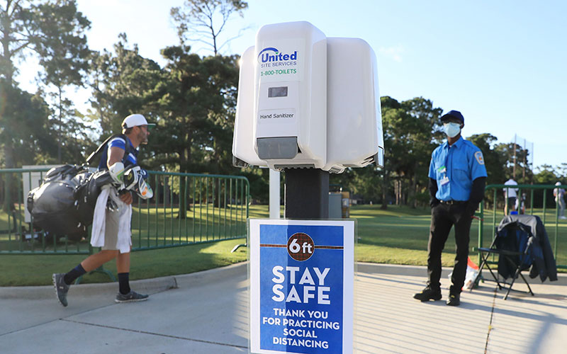 A security guard wearing a face mask looks on near COVID-19 social distancing signage and hand sanitizer at the entrance to the driving range during a practice round prior to the RBC Heritage on June 17, 2020 at Harbour Town Golf Links in Hilton Head Island, South Carolina. (Photo by Streeter Lecka/Getty Images)